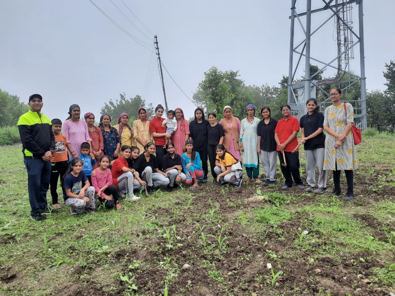 Students and village residents posing together in a green field on a cloudy day, marking community partnership during the MIS Village Immersion Program.
